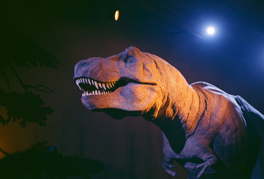 A lifelike T. rex model bathed in dramatic lighting shows sharp teeth and textured skin, evoking a sense of power and ancient mystery.