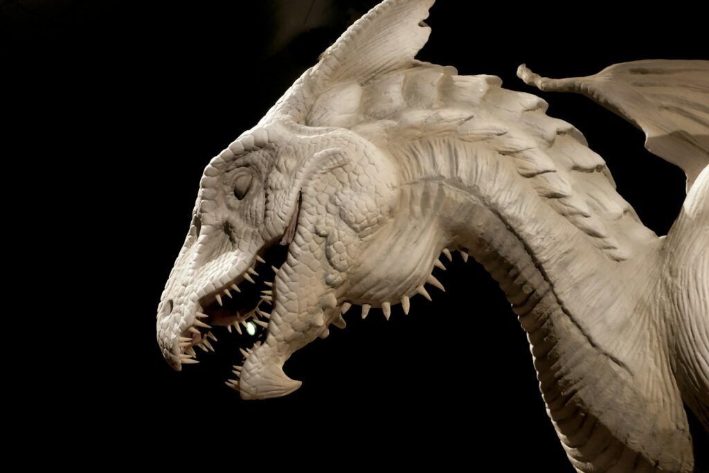 Close-up of a detailed, white dragon sculpture with textured scales and sharp teeth against a black background, conveying a sense of power and mystique.