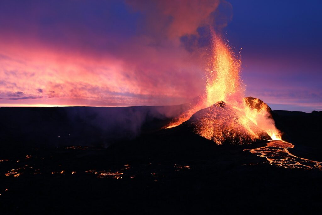 a volcano erupts lava as the sun sets