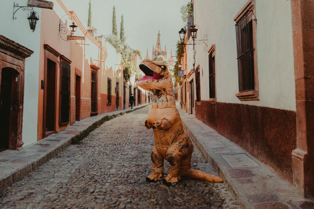 A humorous scene of a person in a dinosaur costume on a cobblestone street in San Miguel de Allende.
