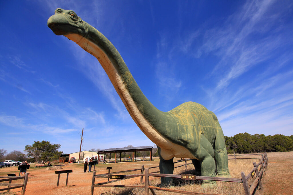 A large green tatue stands prominently under a clear blue sky. The fenced display is set in a grassy area, creating a realistic and playful scene.