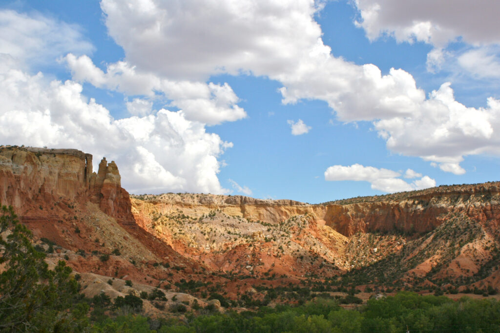 Rocky desert landscape with red and orange cliffs under a bright blue sky dotted with fluffy white clouds, evoking a sense of openness and serenity.