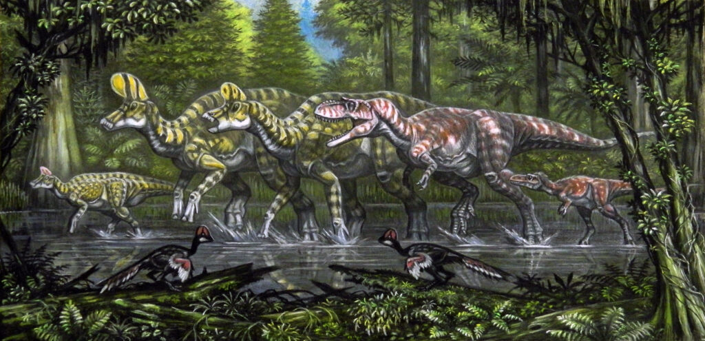 Dinosaurs walking through a prehistoric forest. Two large dinosaurs with crests lead, followed by a smaller carnivorous dinosaur. Two bird-like creatures forage near the water's edge. The scene is lush and ancient.