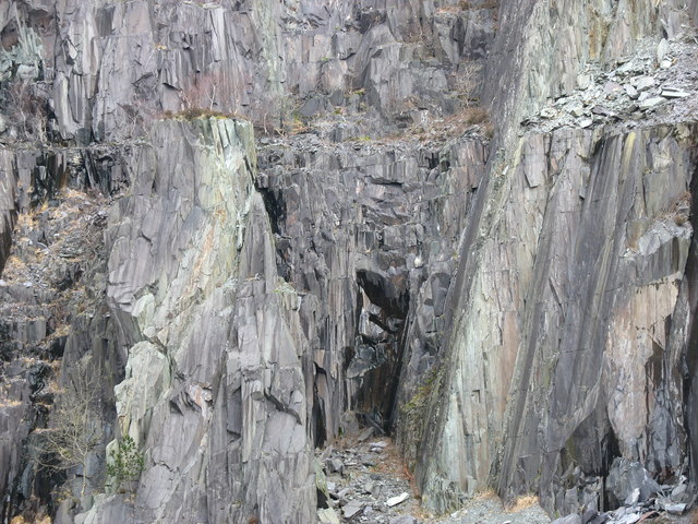 Rugged cliff face with sharp, jagged slate formations. The gray rocks are textured and weathered, creating a dramatic and imposing natural landscape.
