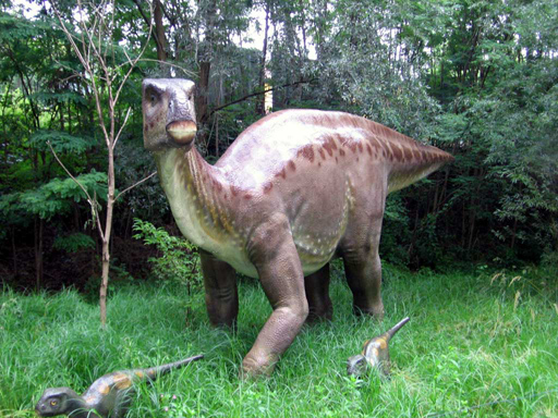 Model of a large dinosaur, resembling a Hadrosaurus, with two smaller dinosaurs in green forest setting. Scene is calm and lifelike.