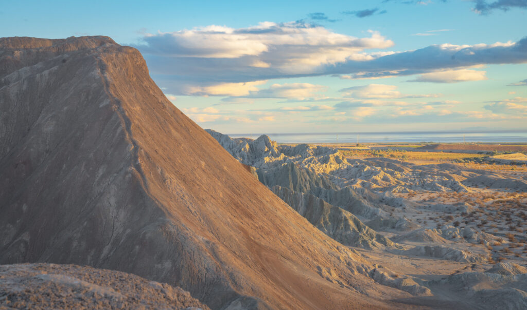 Sunlit mountain landscape with sharp peaks and ridges, casting long shadows. The sky is partly cloudy, adding depth and calm to the scene.