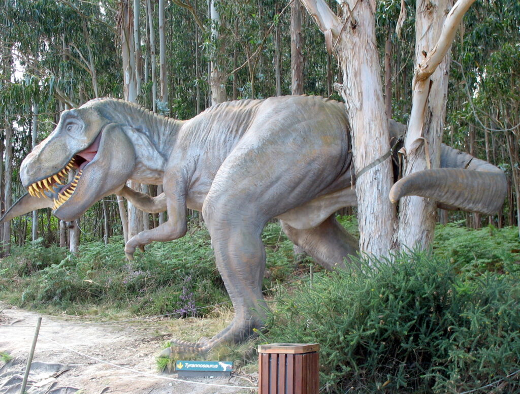 A lifelike T. rex sculpture blends into a lush forest, its open mouth revealing sharp teeth. Its tail curves around a tall tree, adding a dynamic feel.