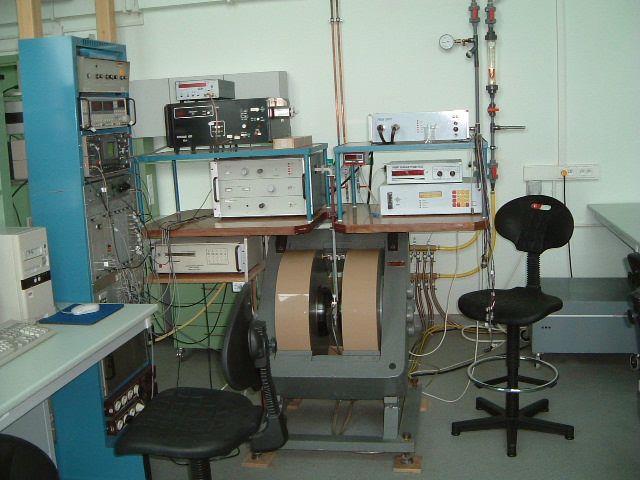 A laboratory with electronic equipment on shelves, including oscilloscopes and meters. Rolling chairs are in the foreground, conveying a high-tech atmosphere.