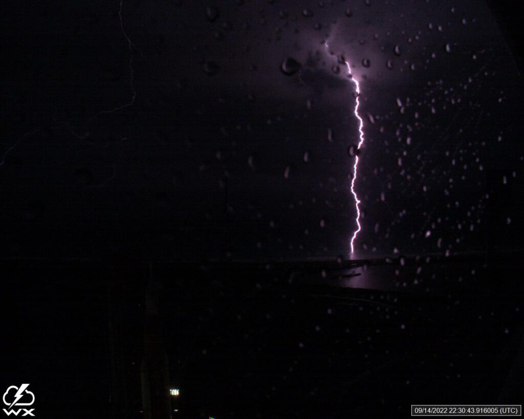 Lightning bolt illuminates a dark night sky, with raindrops visible on a window. The scene conveys a powerful and dramatic atmosphere.
