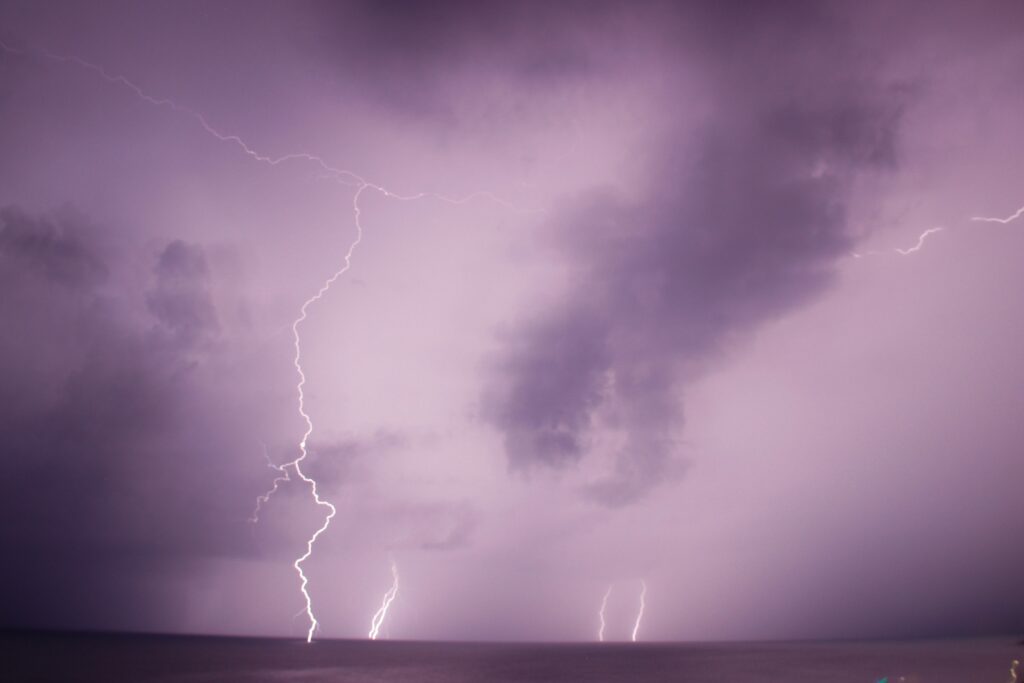 A dramatic scene shows vivid lightning bolts illuminating a stormy purple sky over a dark ocean horizon. The atmosphere is intense and mysterious.