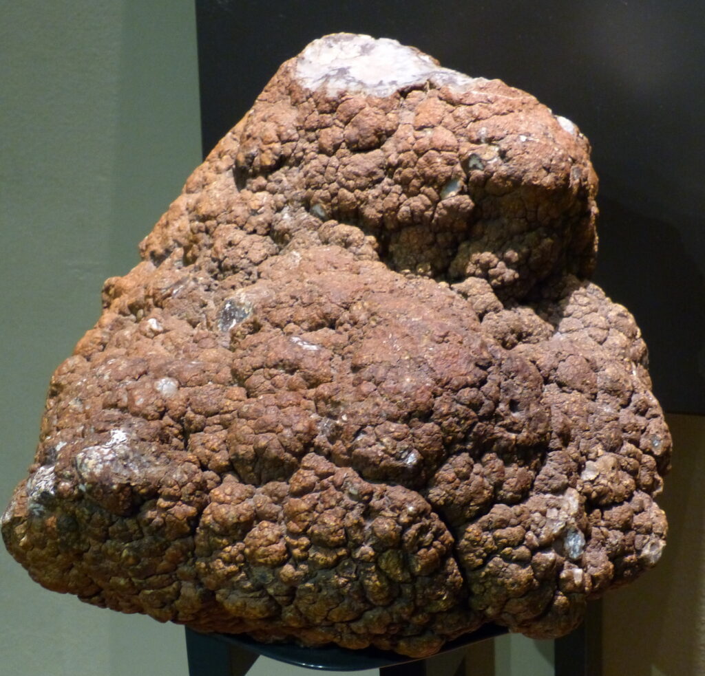 Large brown, textured hematite rock on display against a dark background. Its surface is bumpy, resembling clusters of small, round formations.