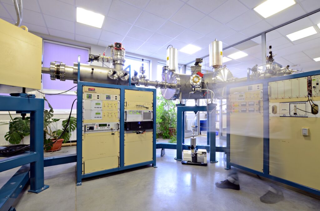 Laboratory setting with complex scientific equipment, including control panels and a vacuum chamber. Blurred motion suggests activity, conveying a dynamic, high-tech environment.