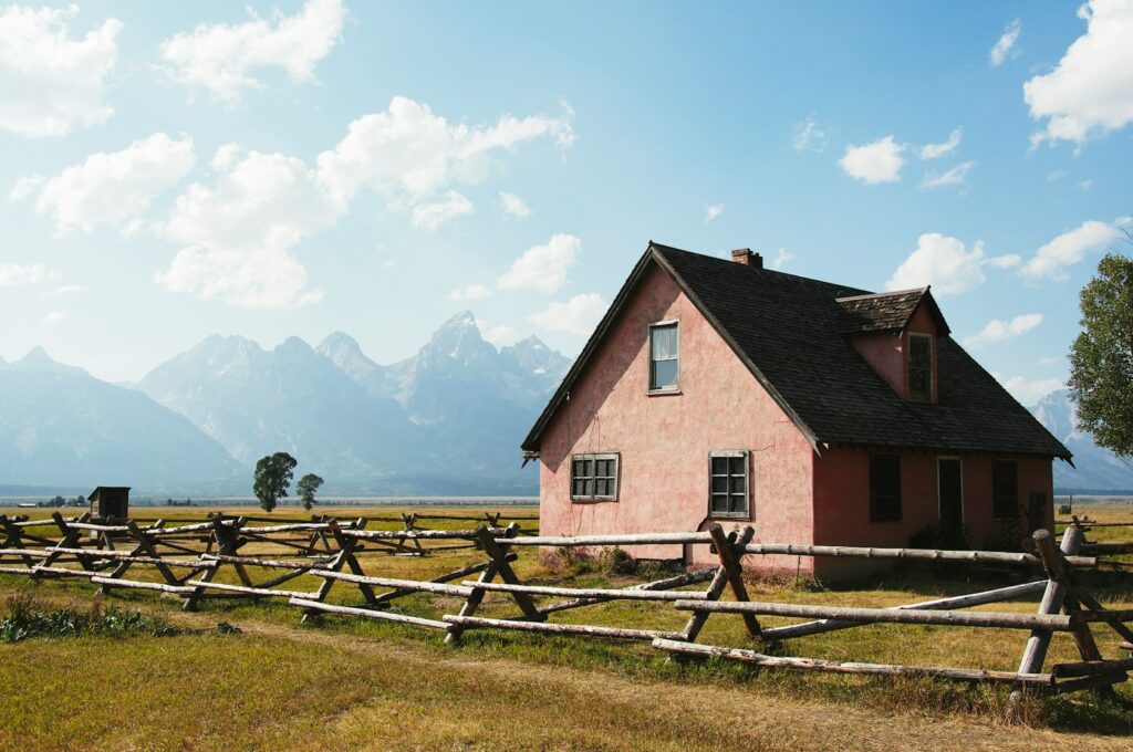 brown and white wooden house on green grass field under white clouds during daytime