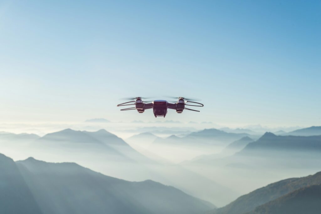 A drone hovers over misty mountain peaks, set against a clear blue sky. The scene conveys tranquility and exploration with its expansive view.