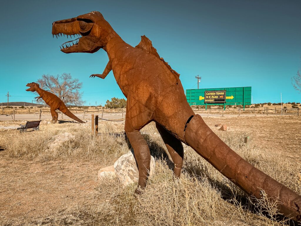 two fake dinosaurs in a field with a building in the background