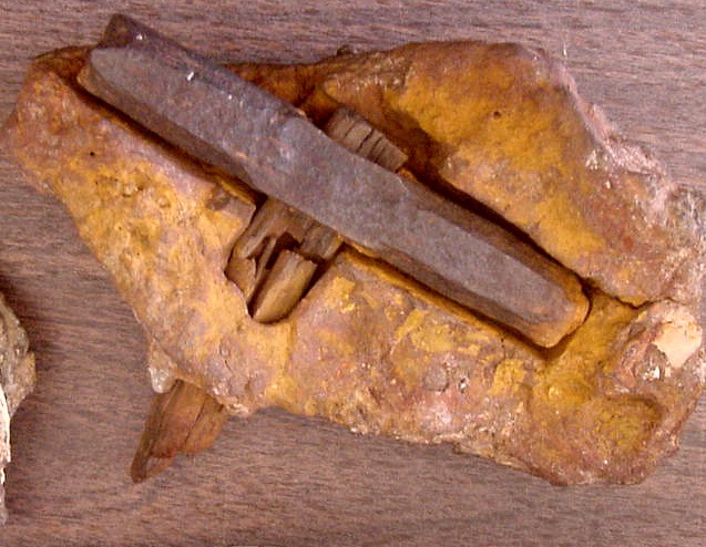 A rusty hammer partially embedded in a rough, brownish-orange rock, suggesting age and weathering. The texture is gritty and earthy.
