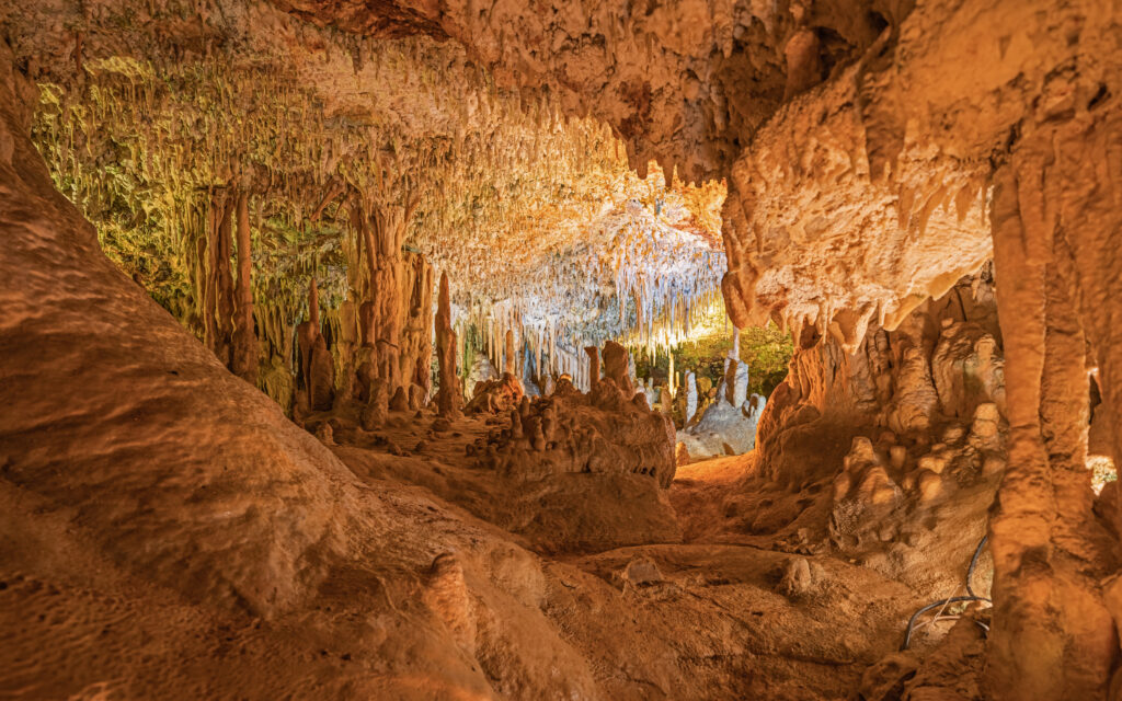 Illuminated cave interior with stunning stalactites and stalagmites, creating an awe-inspiring natural scene. Warm tones and intricate formations.
