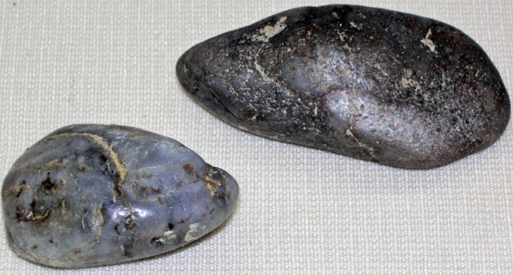 Two smooth, oval-shaped pebbles with a grayish-blue hue and subtle earthy textures sit on a neutral fabric surface, conveying a natural, tranquil tone.