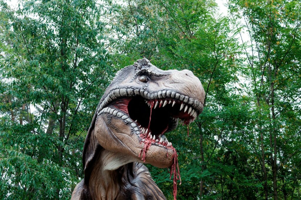 A dinosaur statue with its mouth open in front of trees