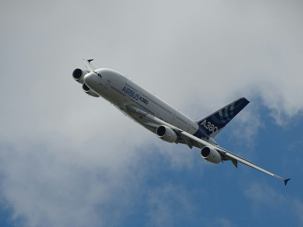 Airbus A380 flying at an angle against a partly cloudy sky. The aircraft's body is highlighted against the blue sky, conveying a sense of power.