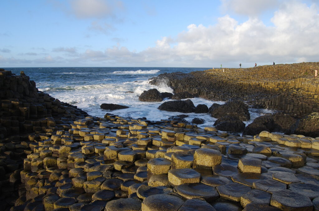 A sweeping ocean view from the edge of rocky cliffs, with waves crashing below and the vast blue horizon stretching into the distance.