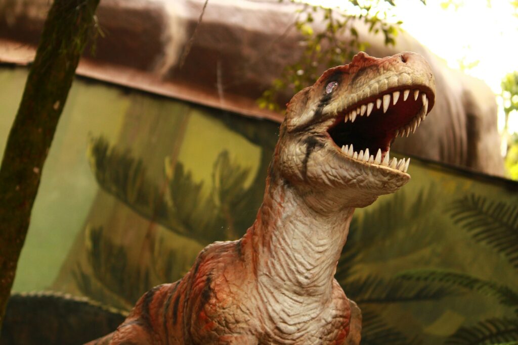 A toy dinosaur with its mouth open in front of a painting