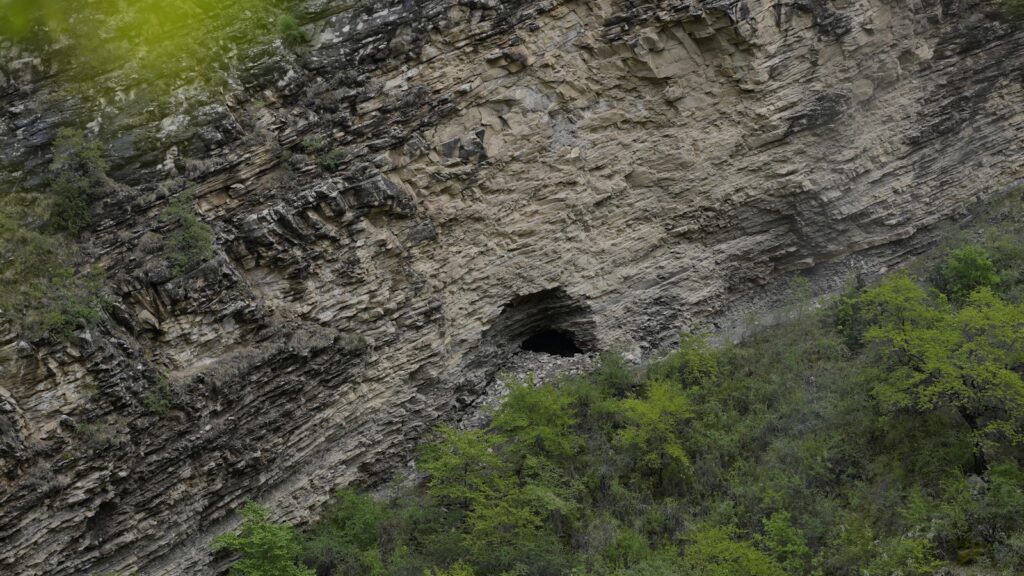 A cave opening sits within a rocky cliffside.