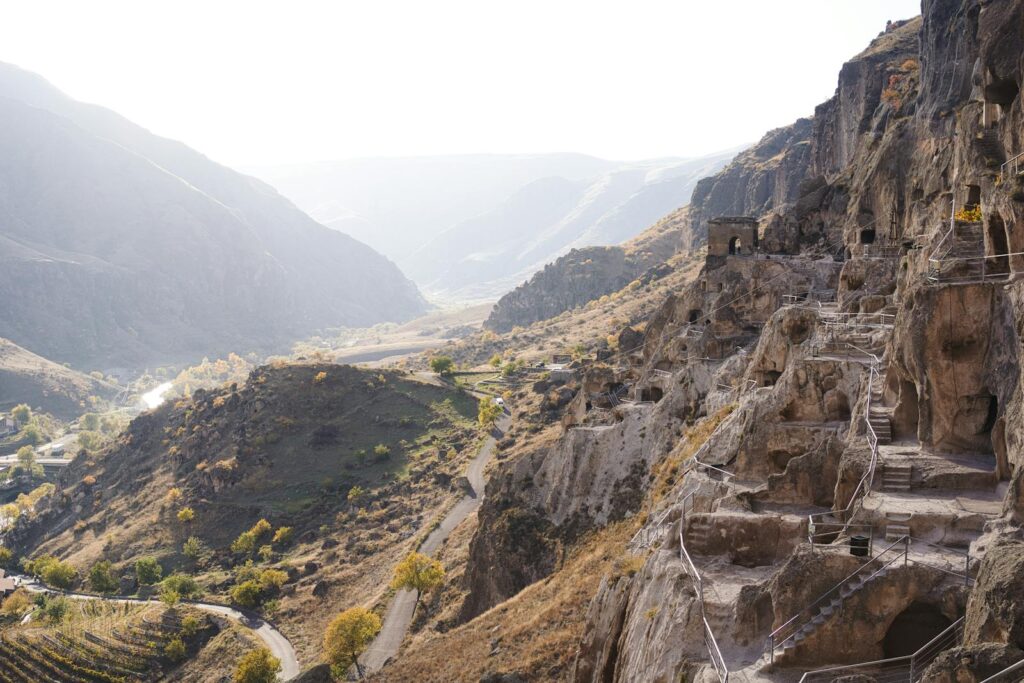 Explore sunlit ancient cave ruins nestled in a scenic valley with distant mountains.